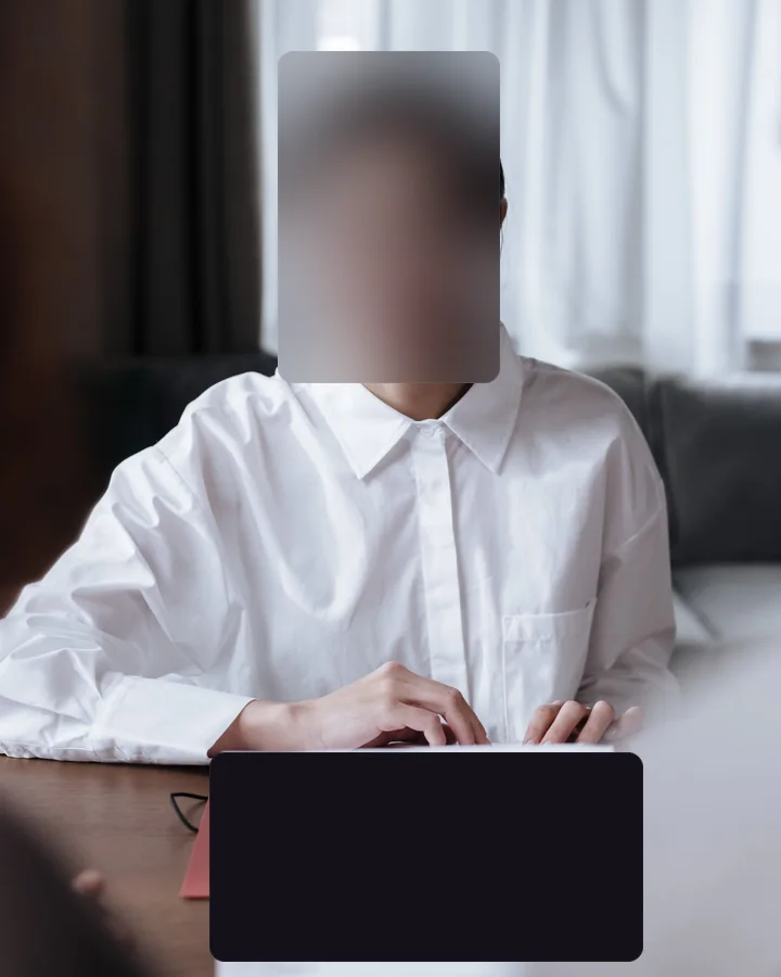 The same frame after redaction: face — primary subject covered with blur, document on desk covered with block.